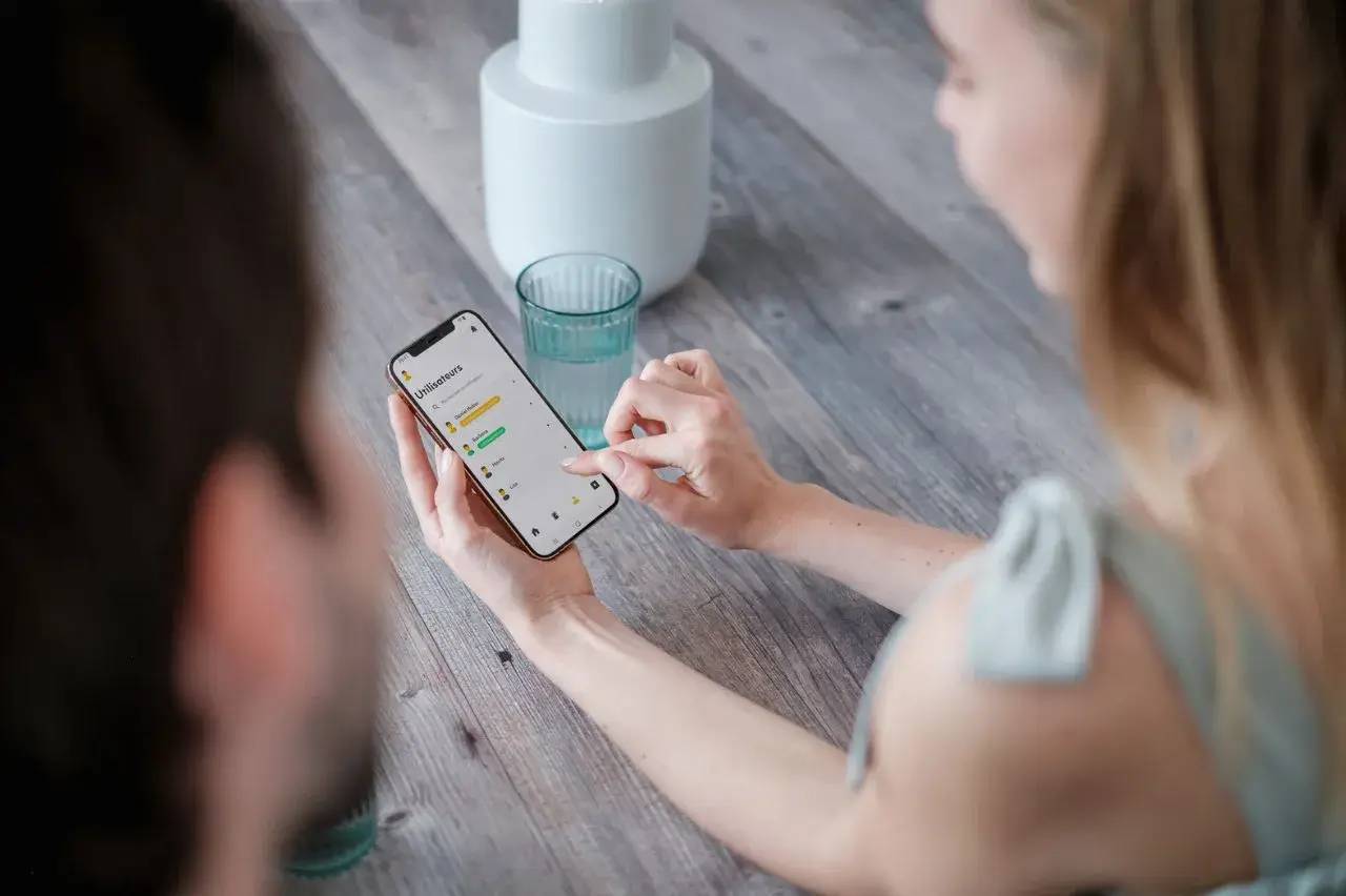 Deux personnes consultent un smartphone avec une interface d'application sur une table en bois.