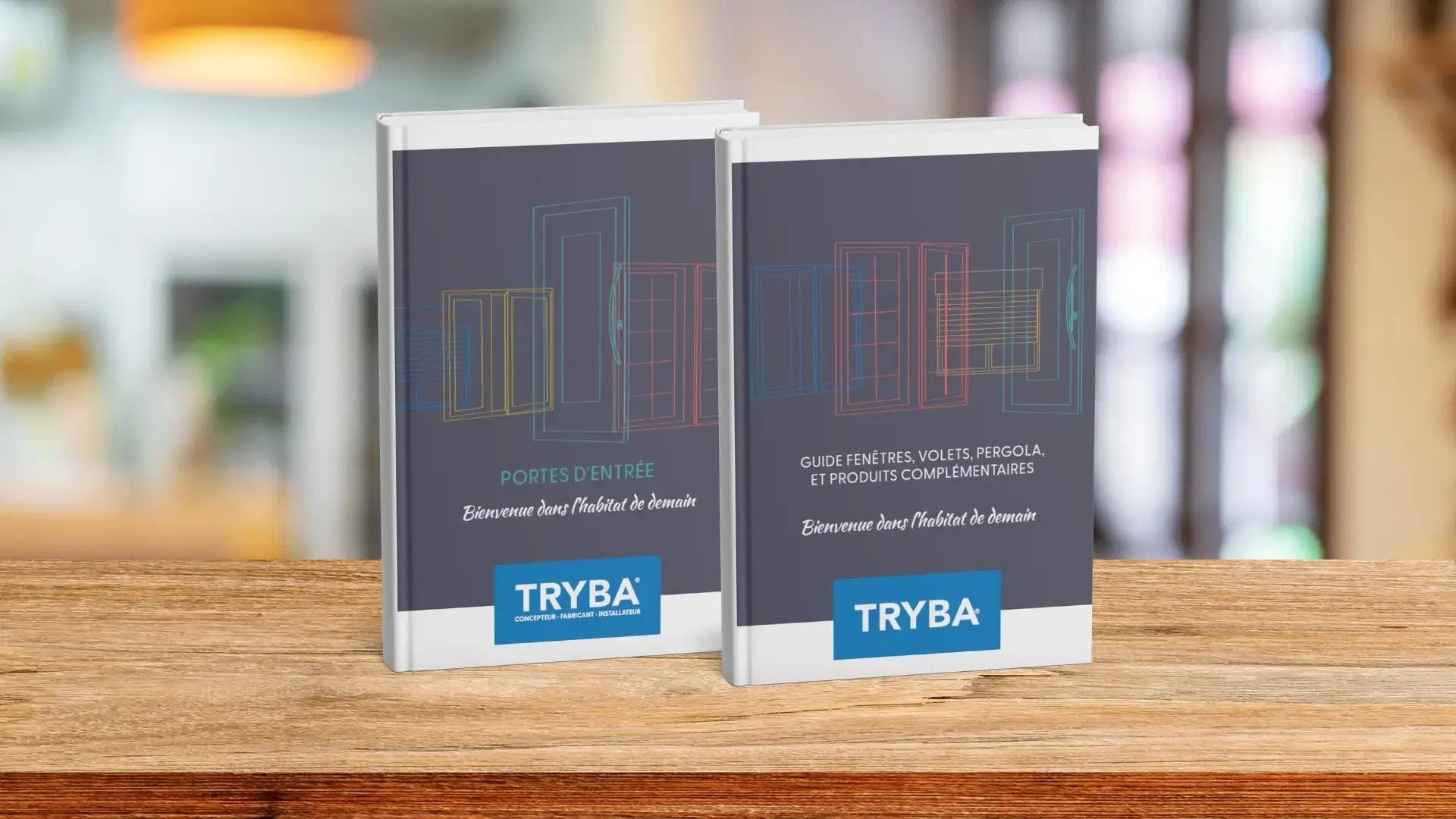 Deux catalogues Tryba sur un bureau en bois, présentant des portes d'entrée et des solutions de fenêtres.