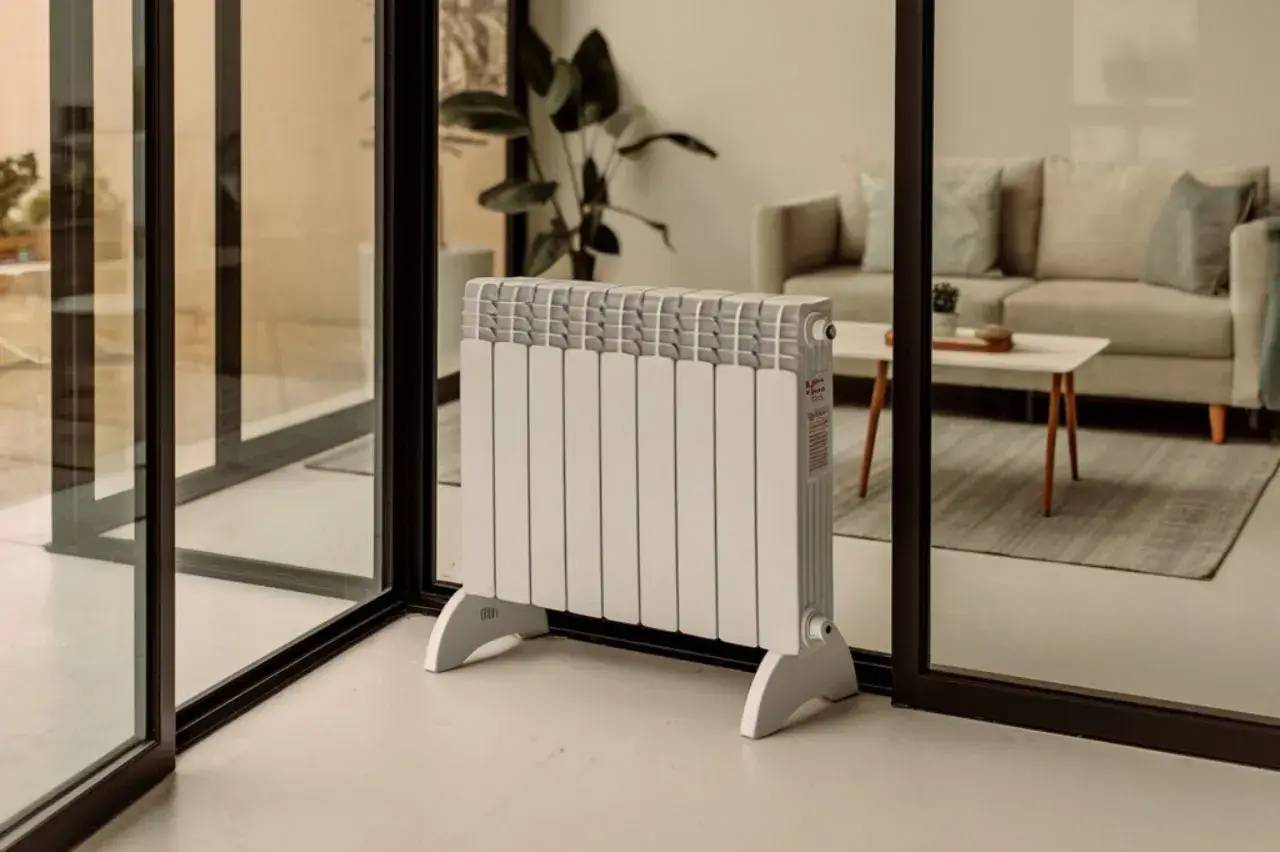 Radiateur électrique blanc moderne devant une grande baie vitrée dans un intérieur contemporain et minimaliste.