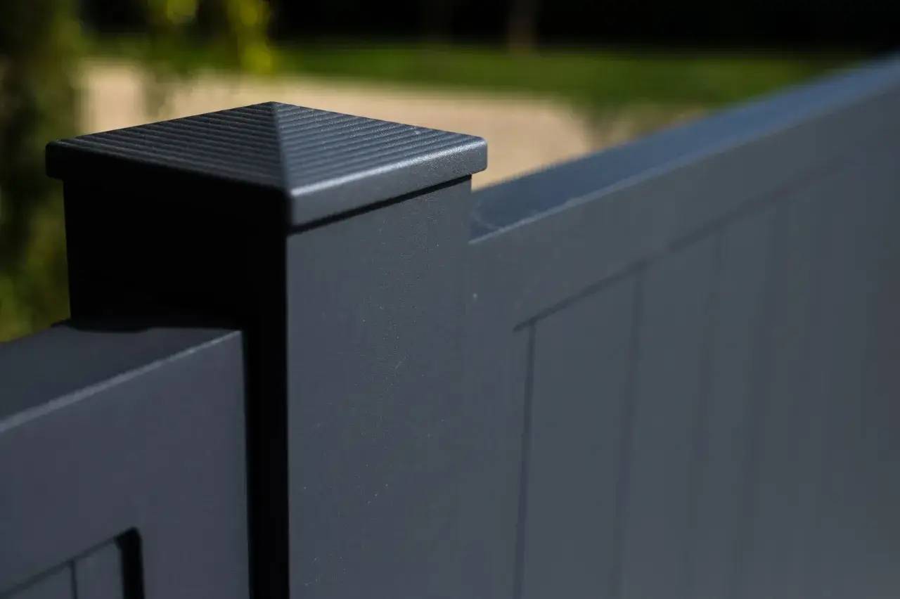 Un gros plan d'un portail moderne en aluminium gris anthracite avec un design épuré et angulaire, dans un environnement extérieur flou.