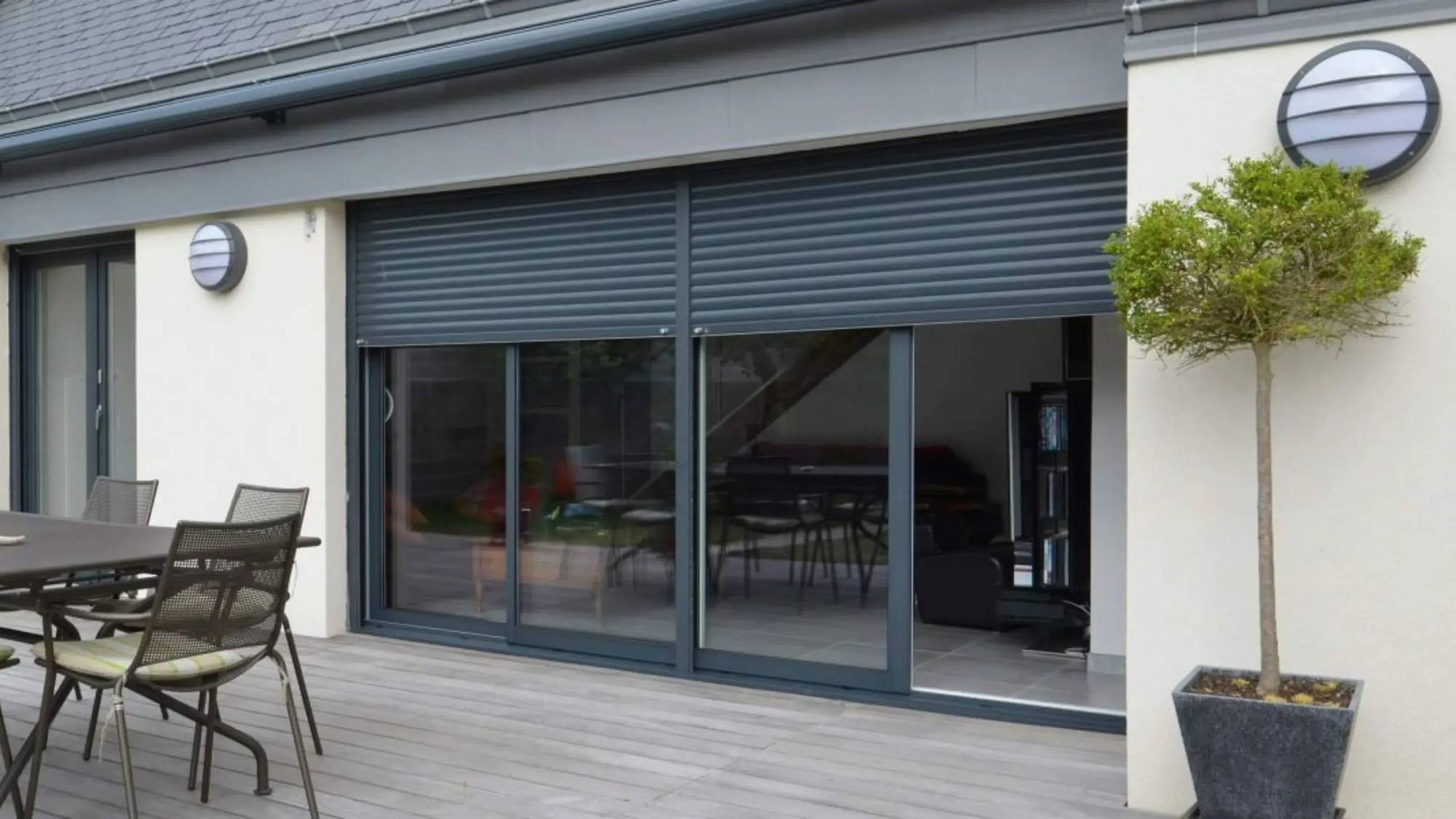 Une terrasse moderne en bois avec des stores roulants fermés devant de grandes baies vitrées.