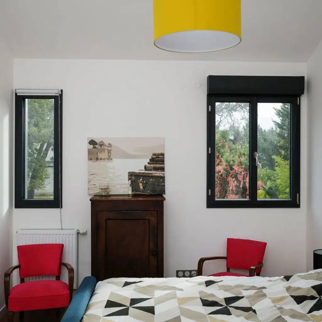 Une chambre lumineuse avec une décoration moderne, comprenant des murs blancs, des touches de rouge et un grand lustre jaune, offre une vue sur la
