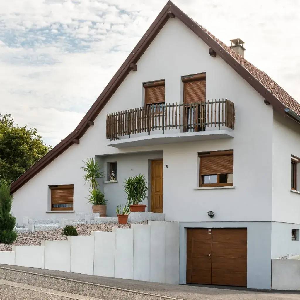 Maison moderne à deux étages avec façade blanche, toit en pente et balcon en bois.