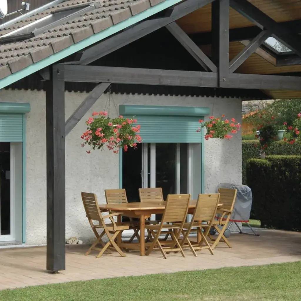 Une terrasse ensoleillée avec un ensemble de mobilier en bois, entourée de verdure et décorée de jardinières suspendues fleuries.