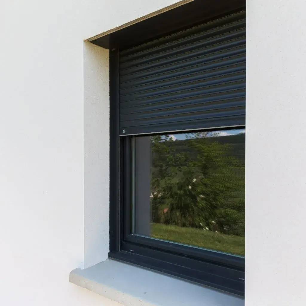 Une fenêtre moderne avec un volet roulant gris foncé partiellement baissé sur une façade blanche.