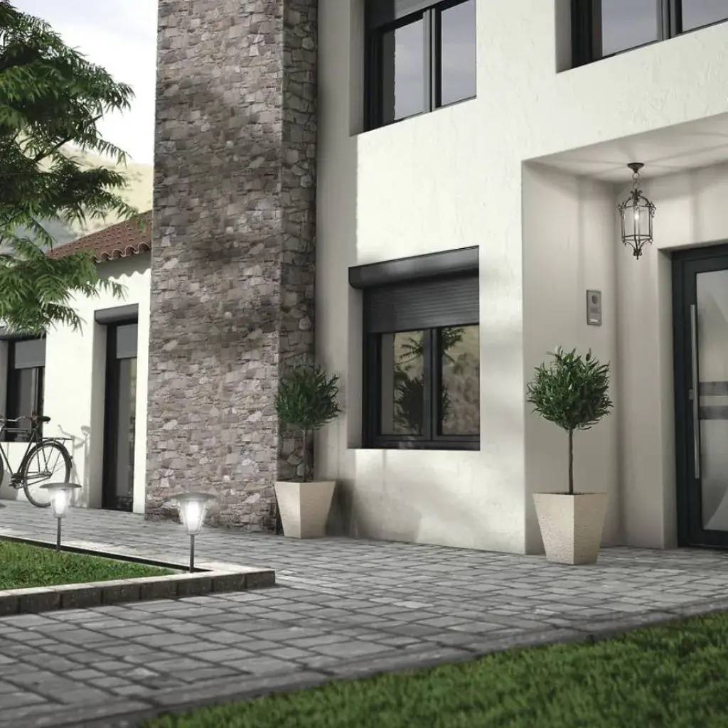 Entrée moderne d'une maison avec façade en pierre, fenêtres noires et pots de plantes décoratifs.