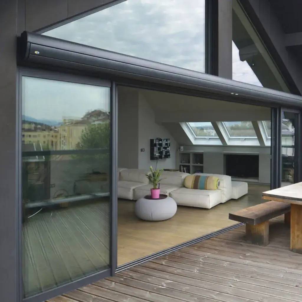 Vue intérieure d'un salon moderne avec de grandes baies vitrées ouvertes sur une terrasse en bois, aménagé avec un canapé et des accents décoratifs