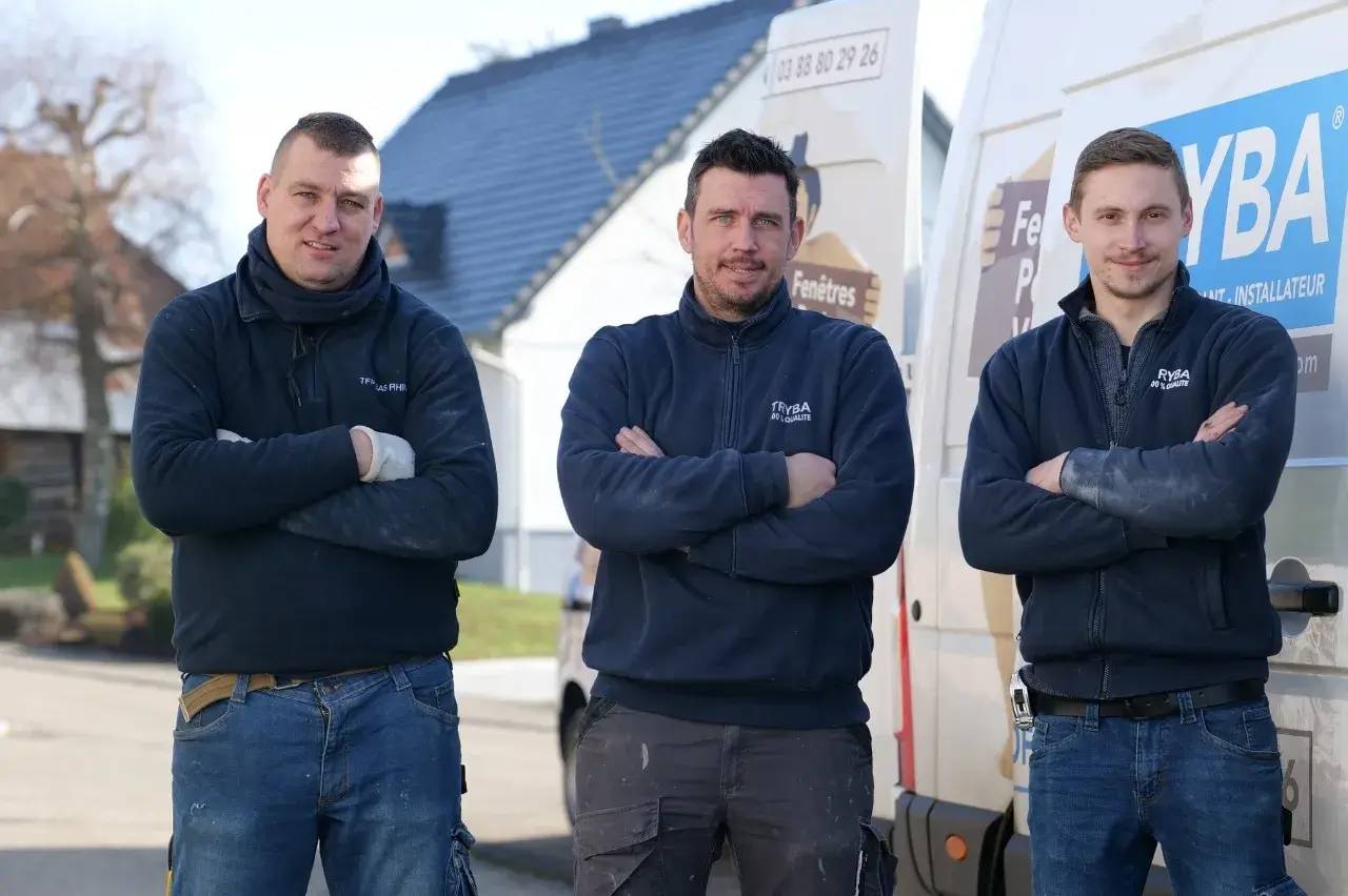 Trois hommes vêtus de pulls "Tryba" posent fièrement devant des véhicules utilitaires de l'entreprise.