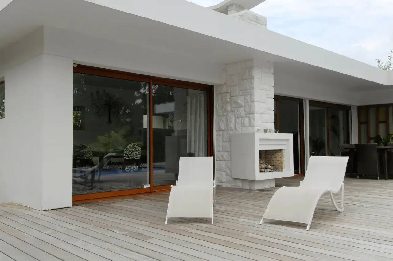 Terrasse moderne avec sol en bois, chaises longues blanches et cheminée extérieure.