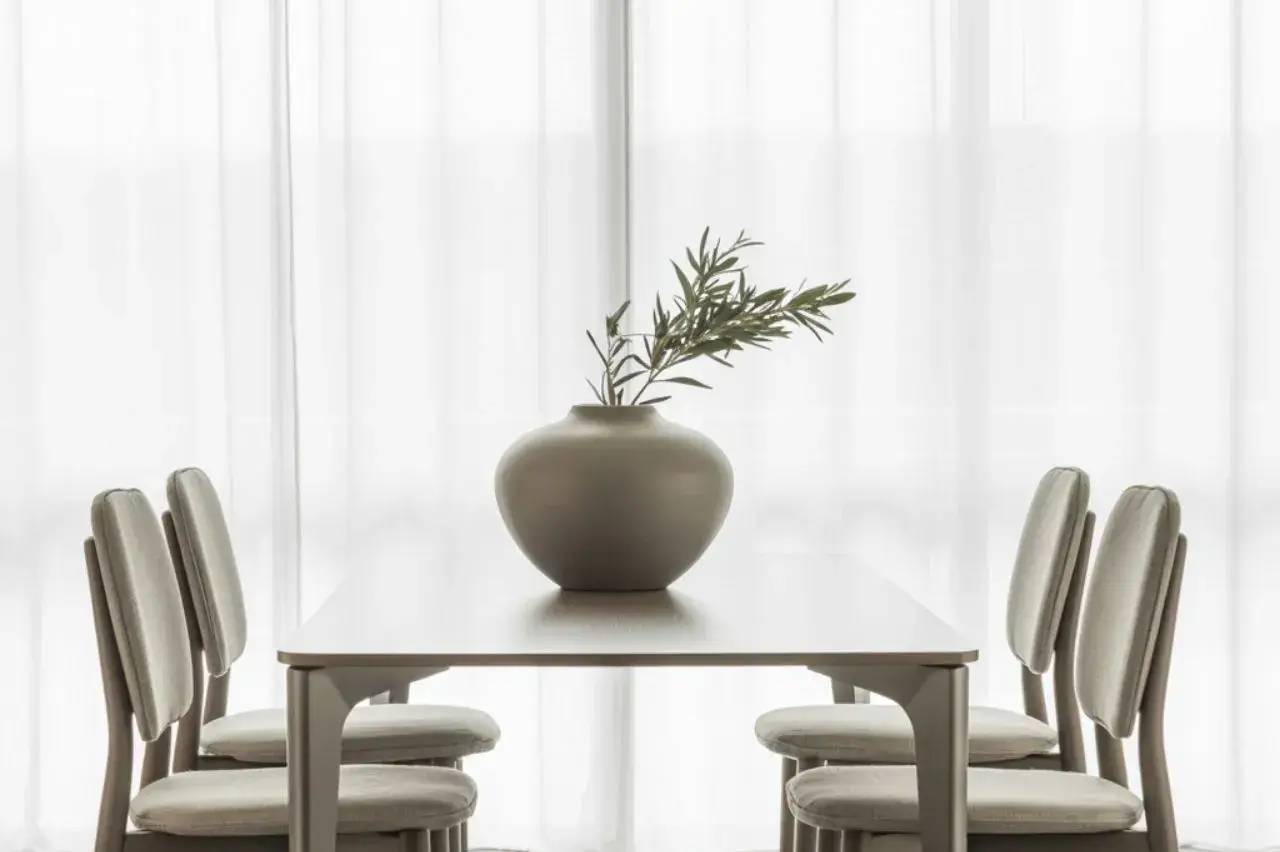 Une salle à manger minimaliste avec une table en bois clair, quatre chaises assorties et un élégant vase contenant des branches vertes.