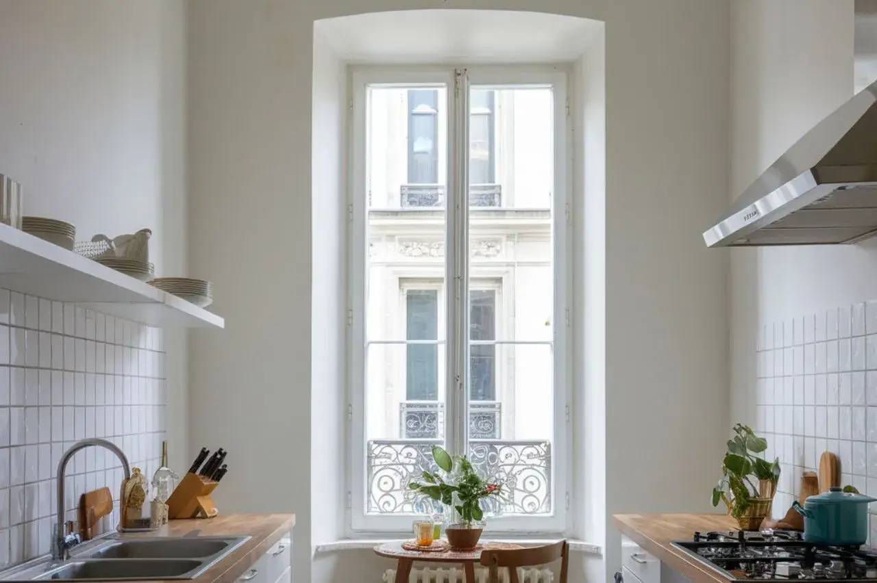 Une cuisine lumineuse et épurée avec un évier moderne, des plans de travail en bois et une grande fenêtre ornée de plantes.