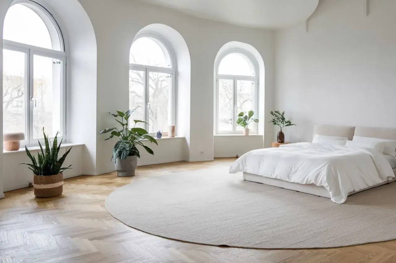 Une chambre lumineuse et minimaliste avec un décor épuré, de grandes fenêtres en arche et des plantes d'intérieur.