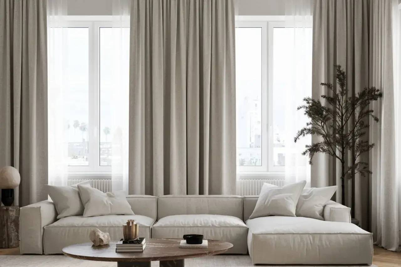 Un salon lumineux et épuré avec un canapé blanc, une table basse en bois et des rideaux beiges, dégageant une ambiance minimaliste