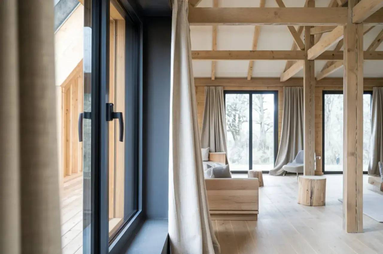 Espace intérieur moderne et lumineux avec de grandes fenêtres, des poutres apparentes en bois, et une décoration minimaliste.