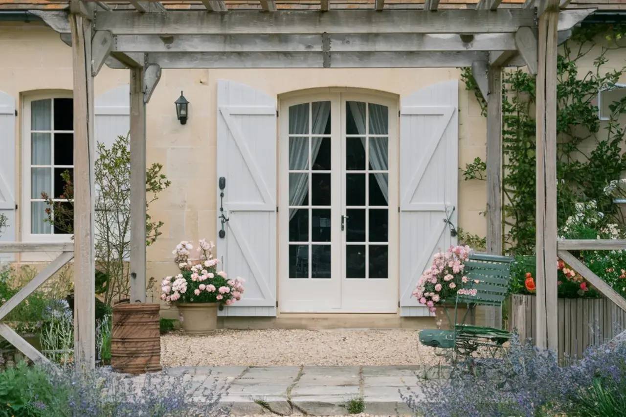 Façade d'une maison charmante avec des volets blancs et un jardin fleuri accueillant.