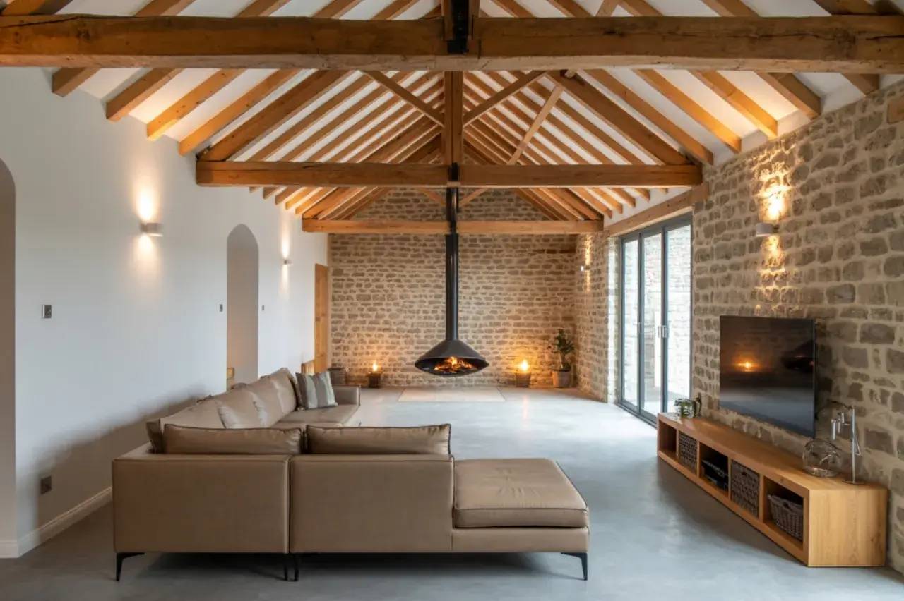 Un salon spacieux mêlant modernité et rusticité avec des murs en pierre apparente, des poutres en bois, une cheminée centrale suspendue