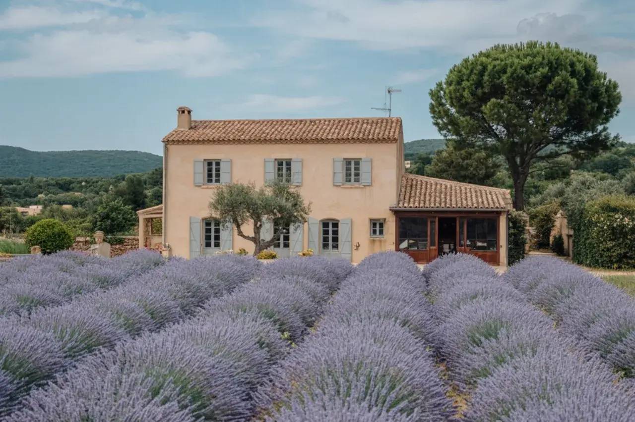 Une maison en pierre au toit de tuiles se dresse au milieu d'un champ de lavande, entourée d'arbres verdoy