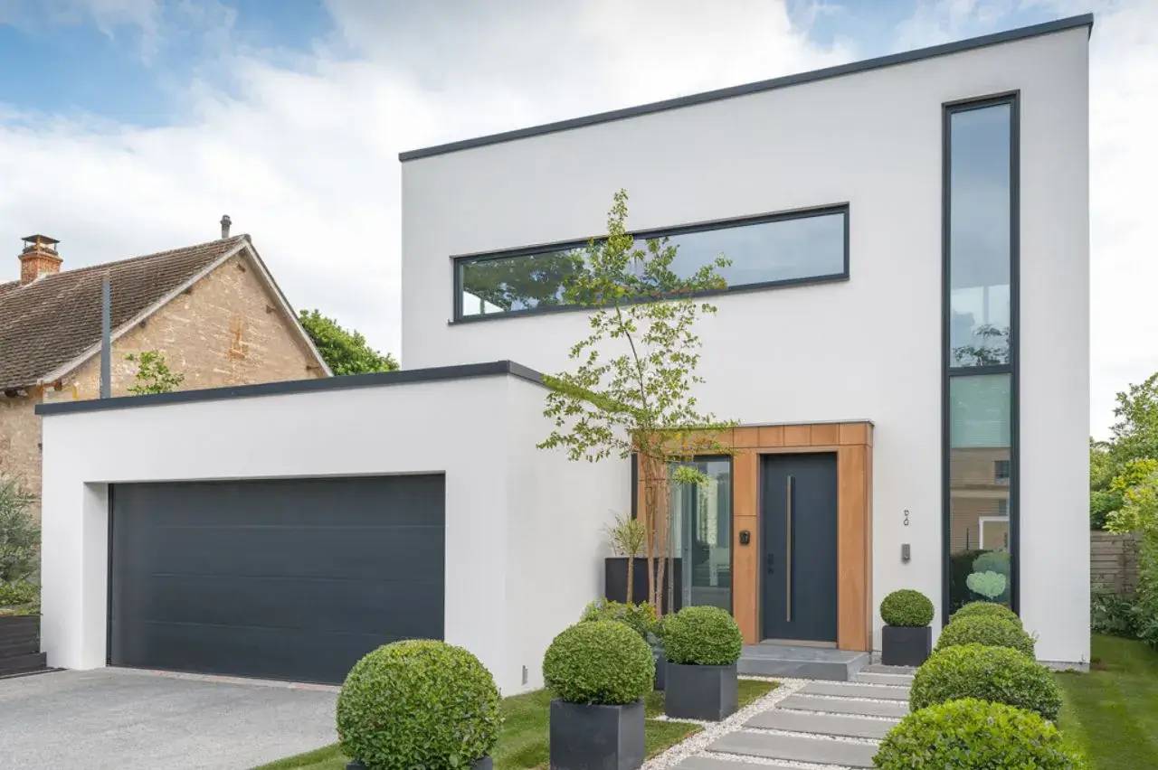 Maison contemporaine à façade blanche avec porte en bois, grandes fenêtres et jardin bien entretenu.