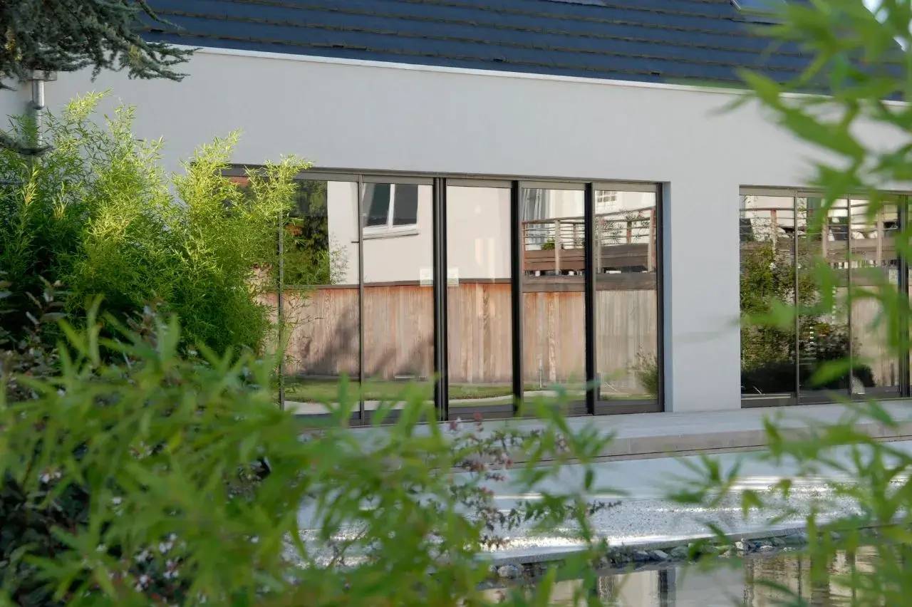 Vue d'une façade moderne avec de grandes baies vitrées entourée de verdure luxuriante.
