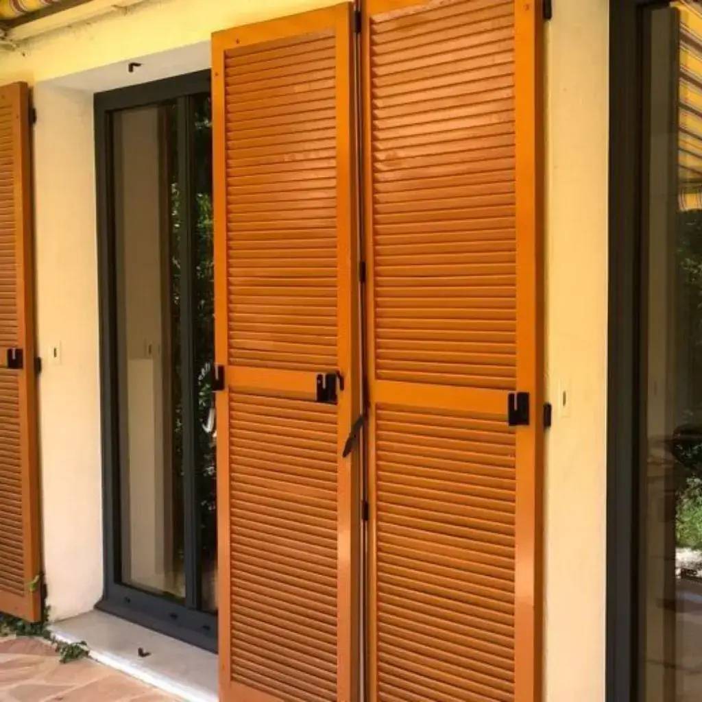 Des volets en bois orange, parfaitement ajustés à une fenêtre moderne, ajoutant une touche chaleureuse à l'extérieur de la maison.
