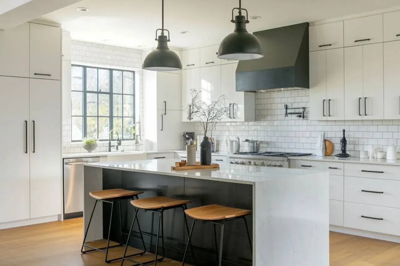 Cuisine moderne et lumineuse avec un îlot central en marbre blanc, des tabourets en bois, et des suspensions noires.