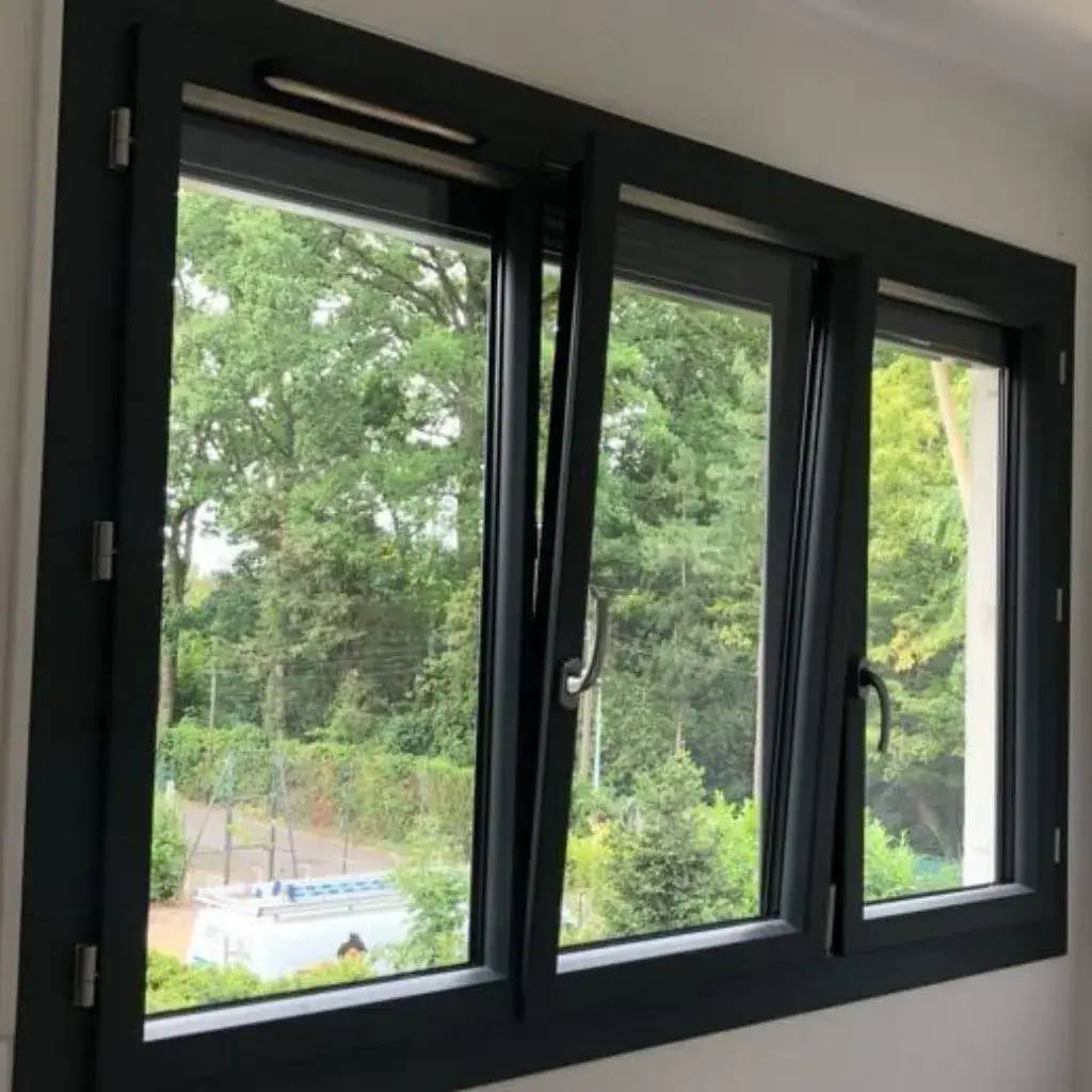 Une fenêtre moderne à cadre noir avec des sections ouvrantes, offrant une vue sur un jardin verdoyant.