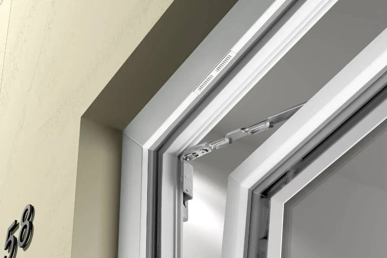 Cette image montre le gros plan d'une fenêtre inclinée avec un cadre blanc et une charnière métallique.