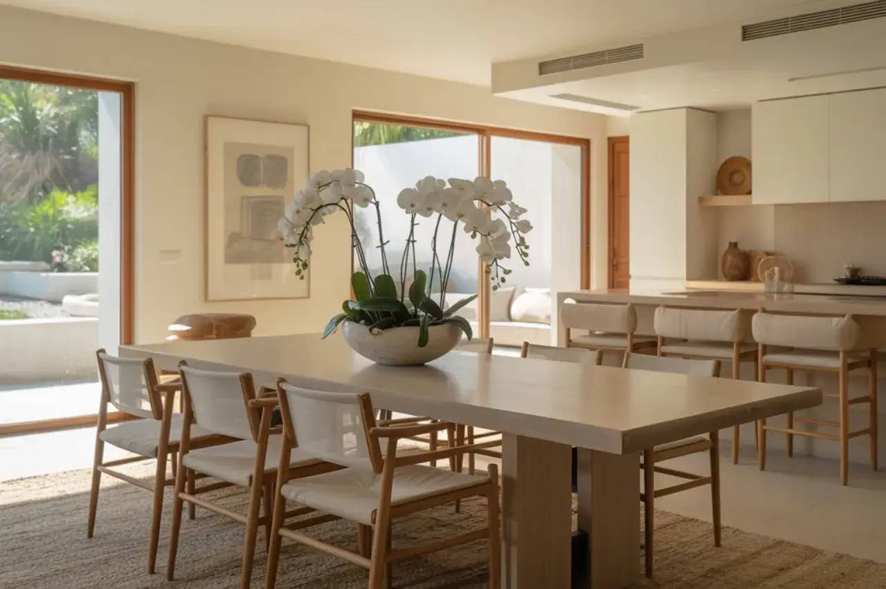 Un salon moderne et lumineux avec une grande table à manger en bois clair, entourée de chaises au design épuré, ornée d'une plante
