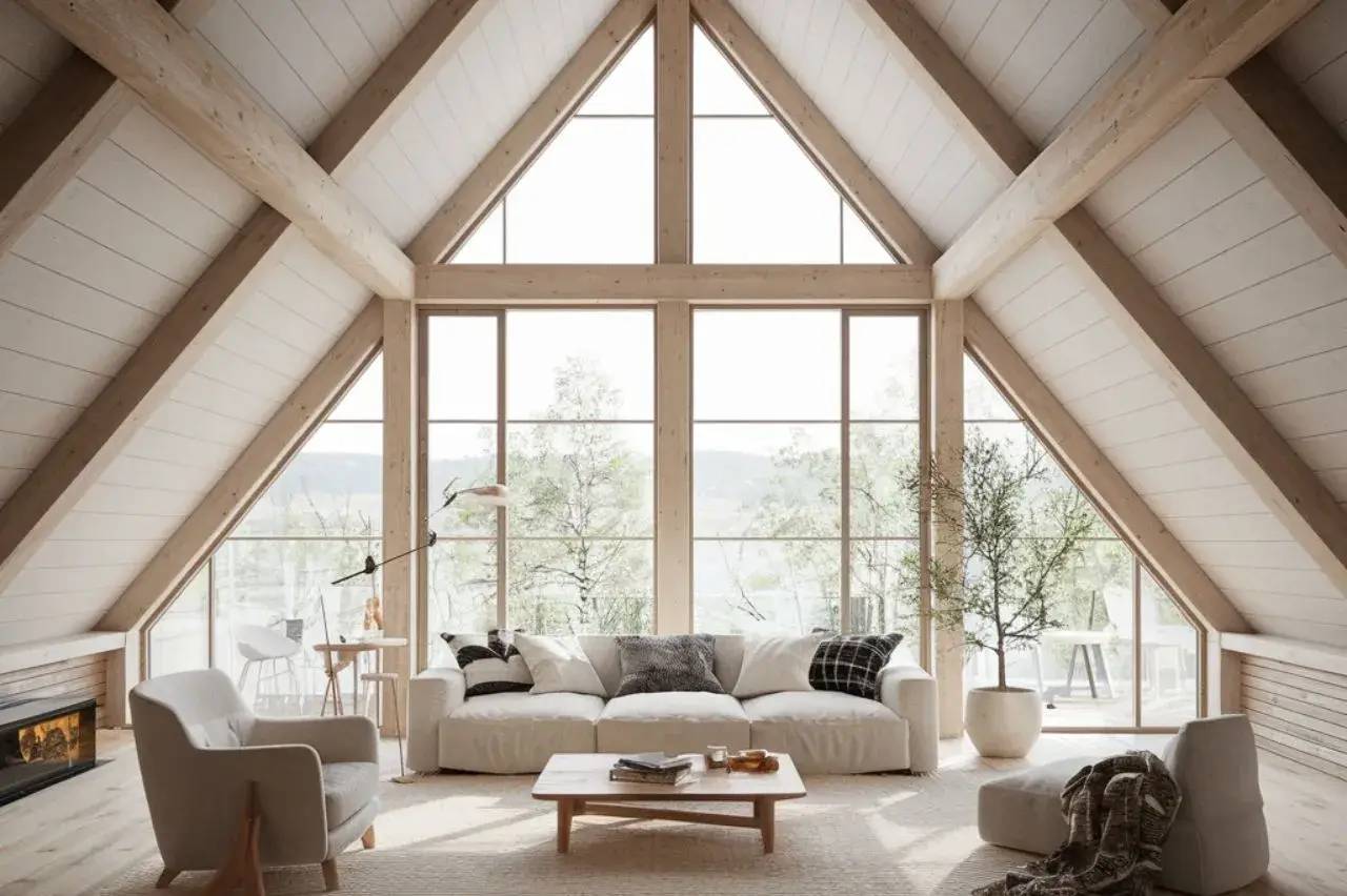 Un salon lumineux avec de hauts plafonds en pente, de grandes fenêtres, et une décoration épurée en bois clair et blanc.