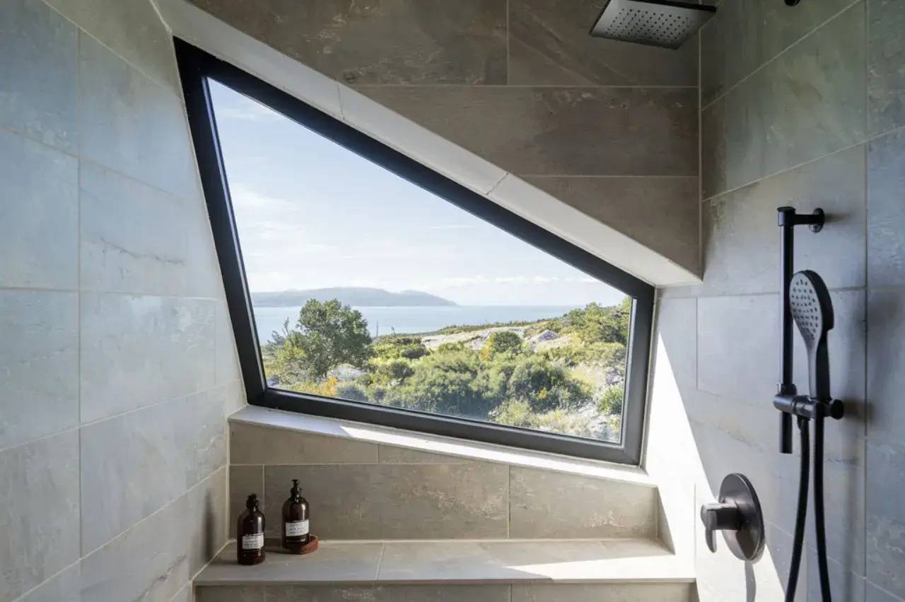 Fenêtre géométrique dans une salle de bain moderne offrant une vue panoramique sur un paysage naturel verdoyant.