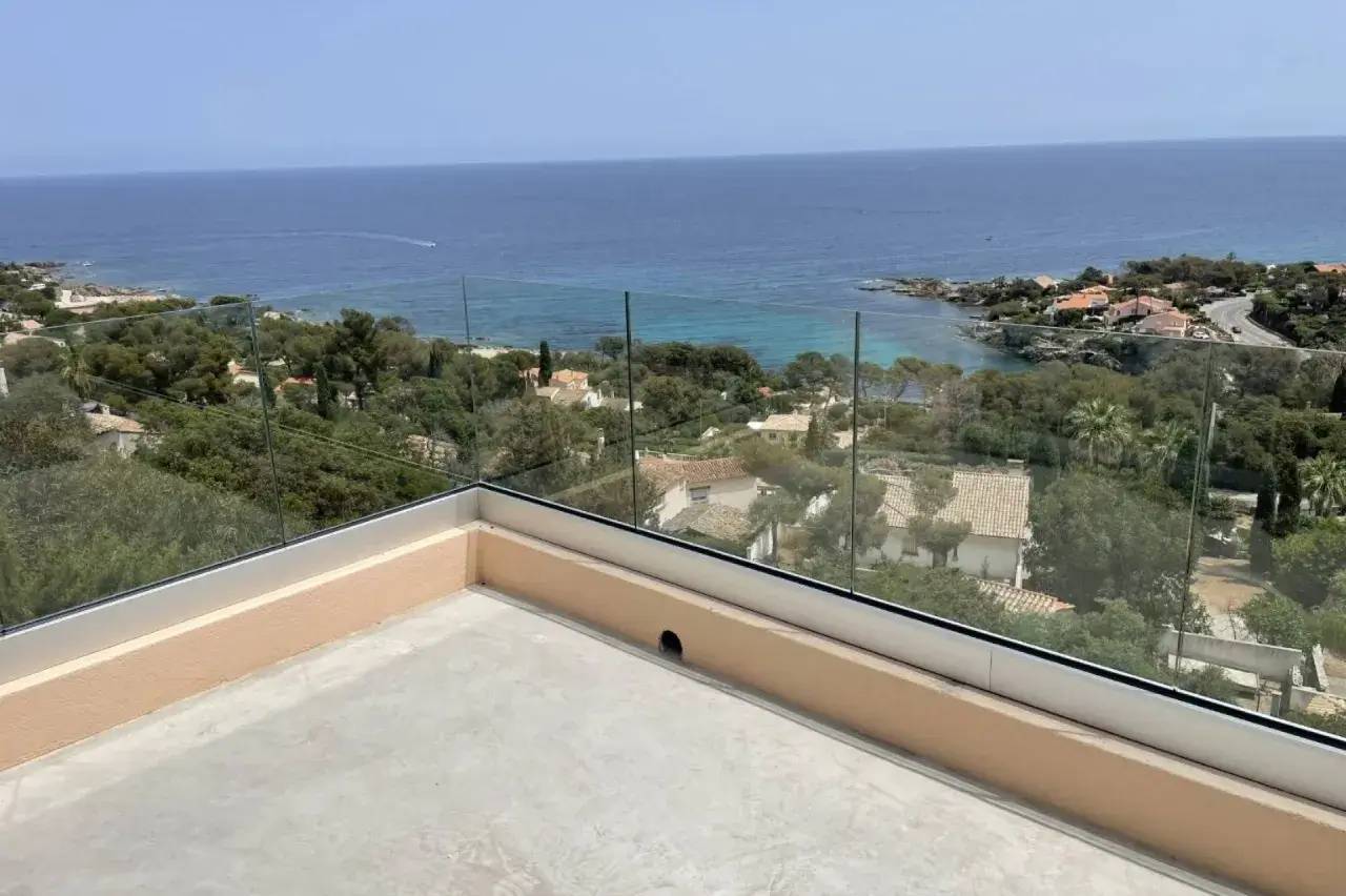 Vue imprenable depuis une terrasse surplombant la mer et les collines verdoyantes.