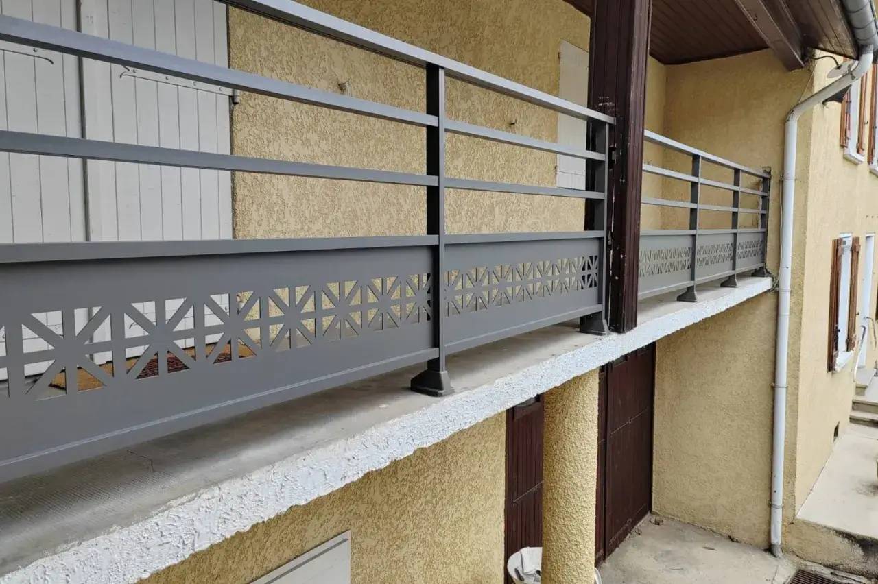Une balustrade métallique moderne et élégante protège un balcon avec une base ornée de motifs géométriques.