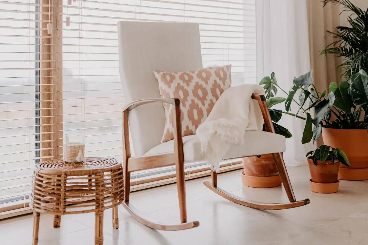 Une chaise berçante en bois avec un coussin à motifs et une couverture blanche est placée près d'une table basse en osier et de