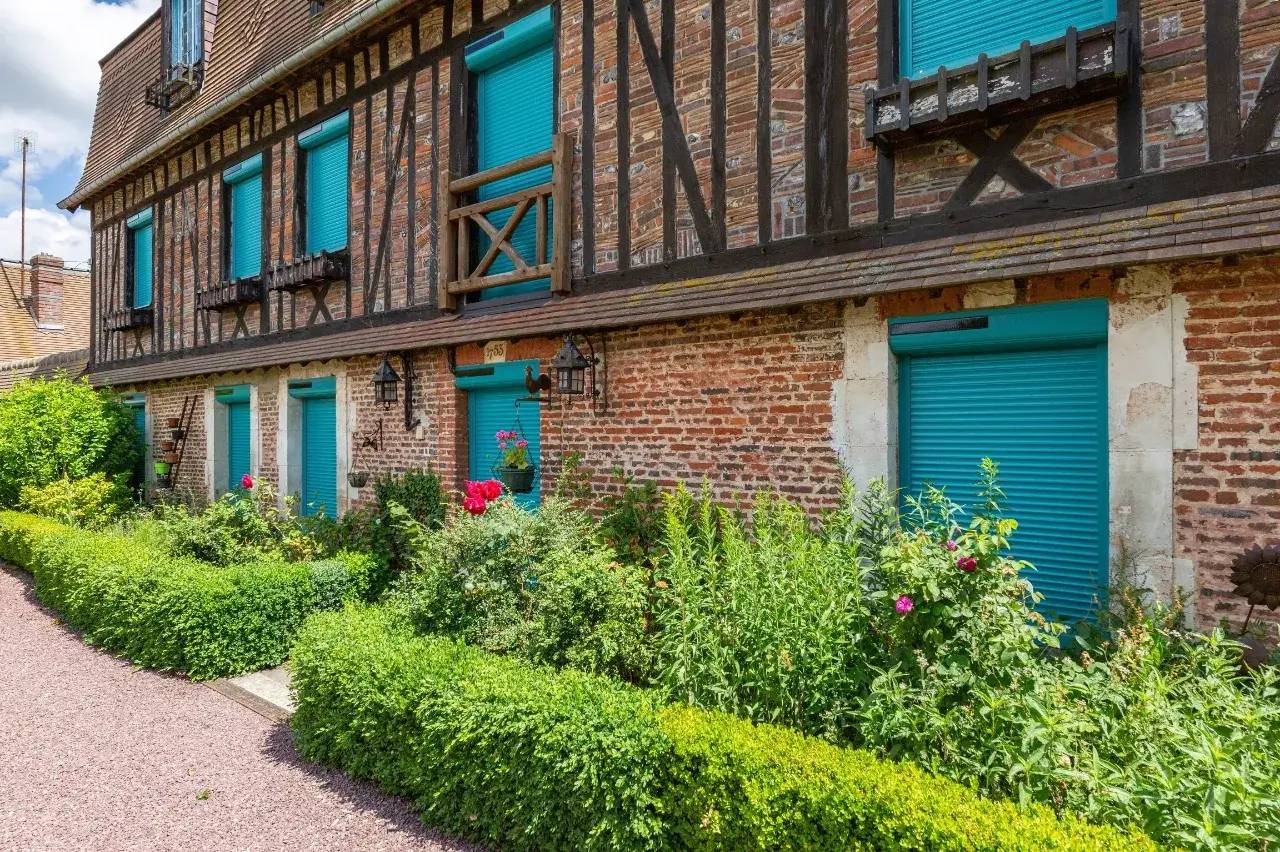 Une charmante maison à colombages avec des volets turquoise et un jardin fleuri luxuriant.