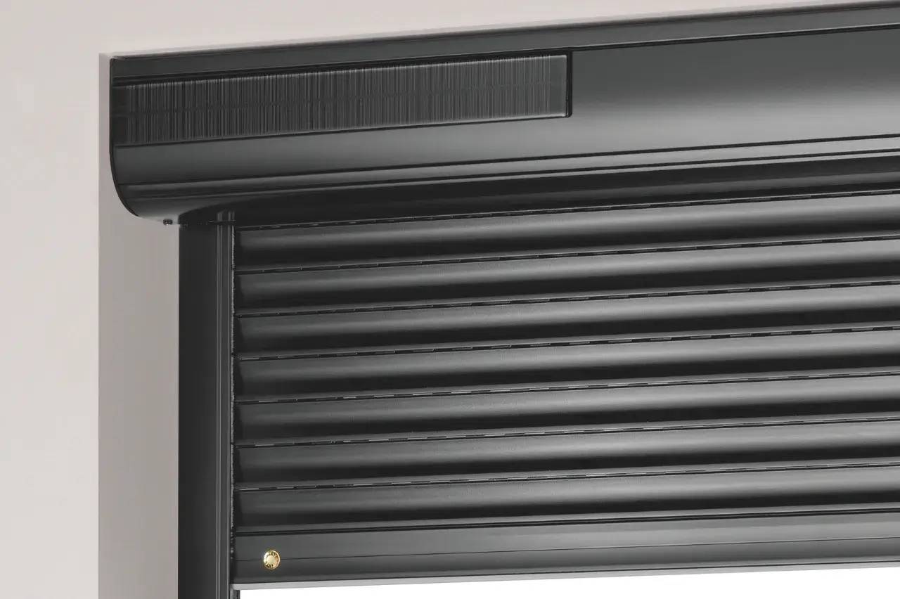 Volet roulant noir avec un panneau solaire intégré sur un mur blanc.