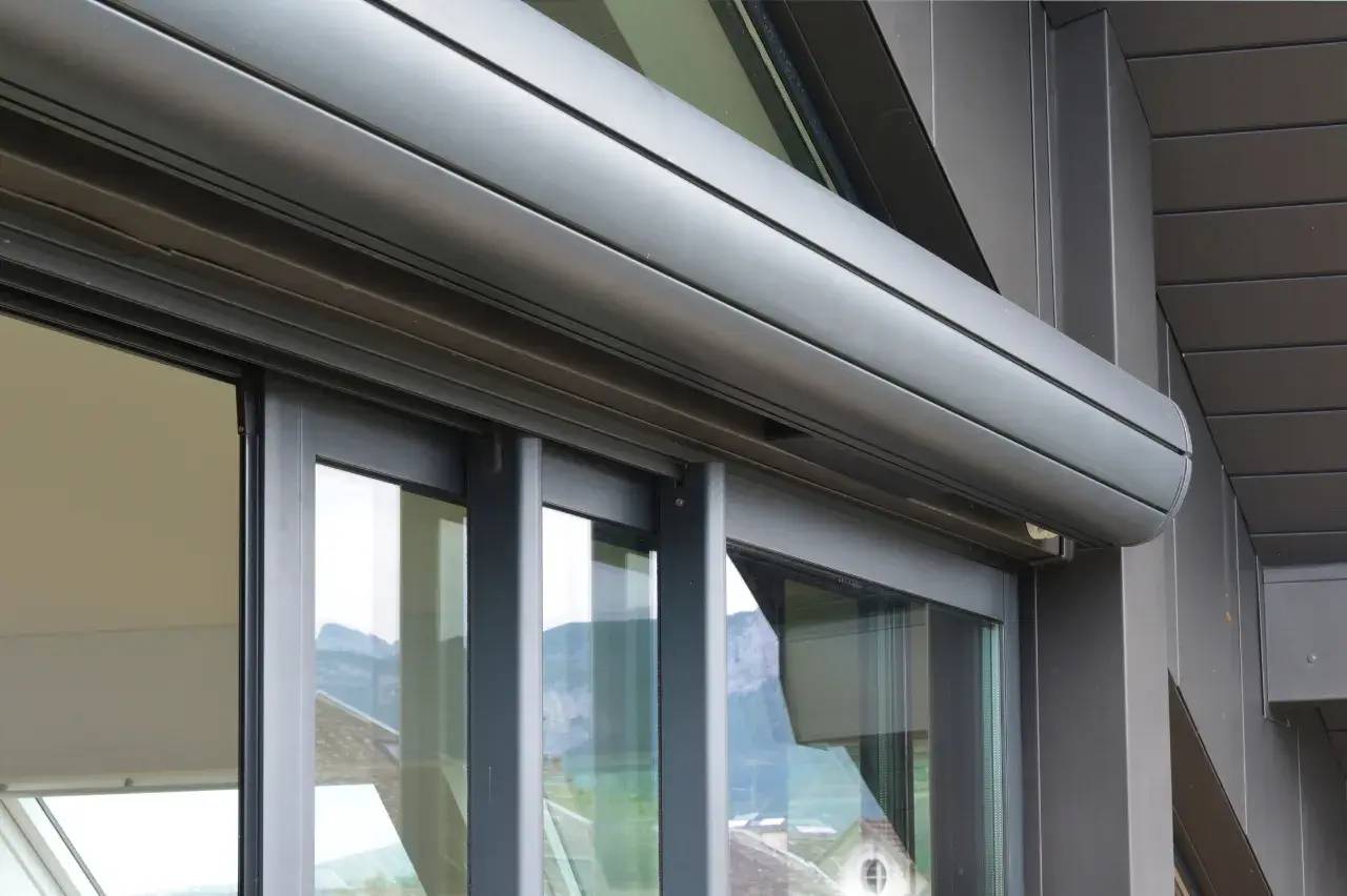 Gros plan sur une architecture moderne avec des fenêtres en verre et un store en métal intégré.