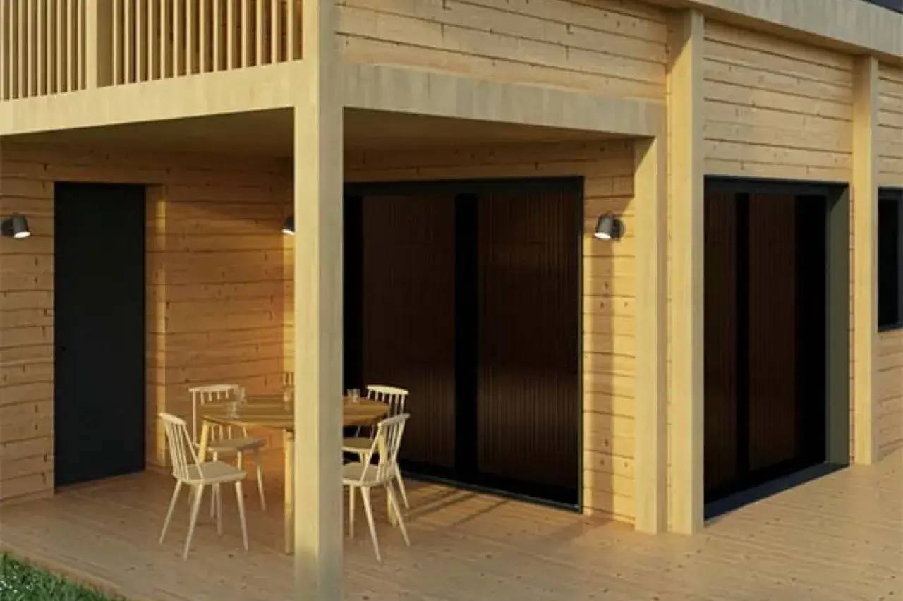 Une terrasse en bois couverte avec une table et des chaises, adossée à un bâtiment moderne équipé de grandes baies vitrées.
