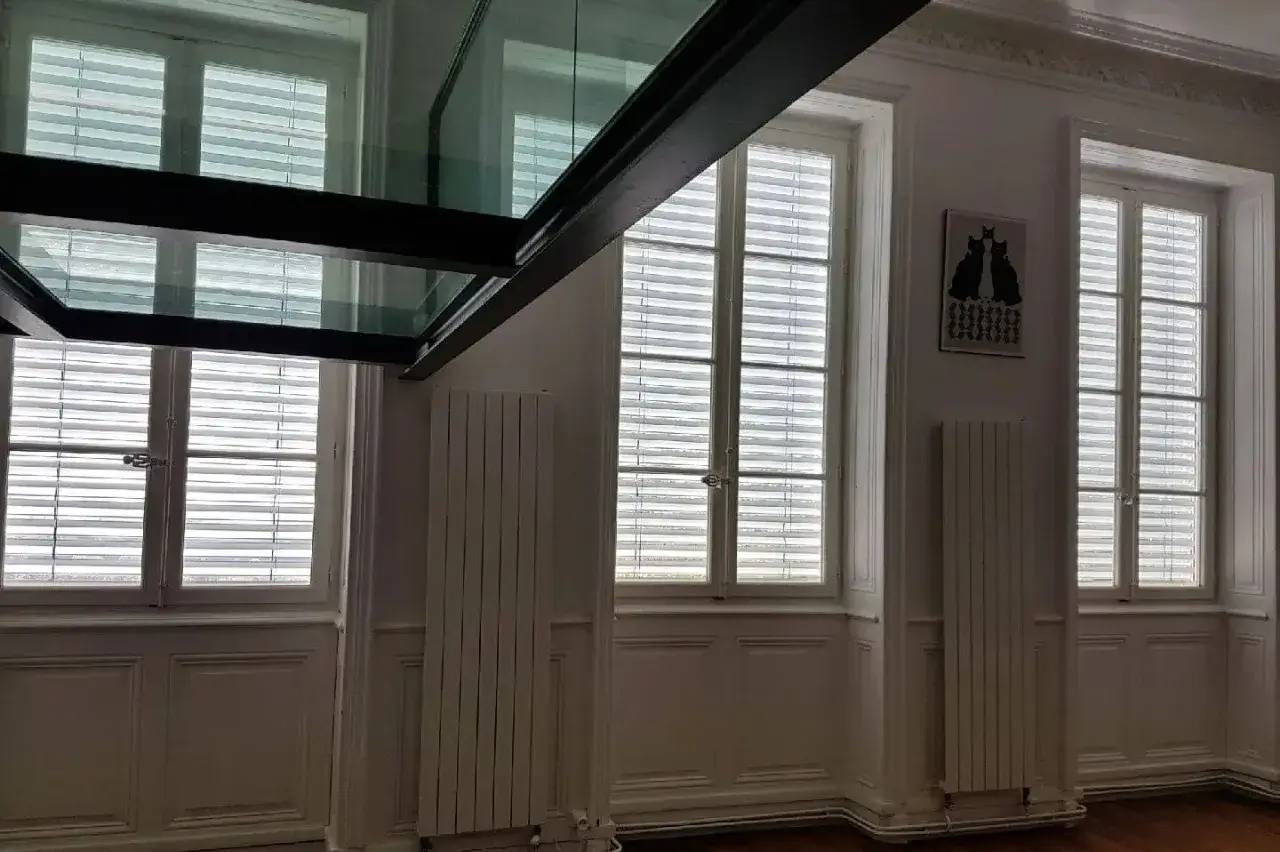 Un intérieur lumineux avec des fenêtres à persiennes blanches et un plancher en verre suspendu au plafond.