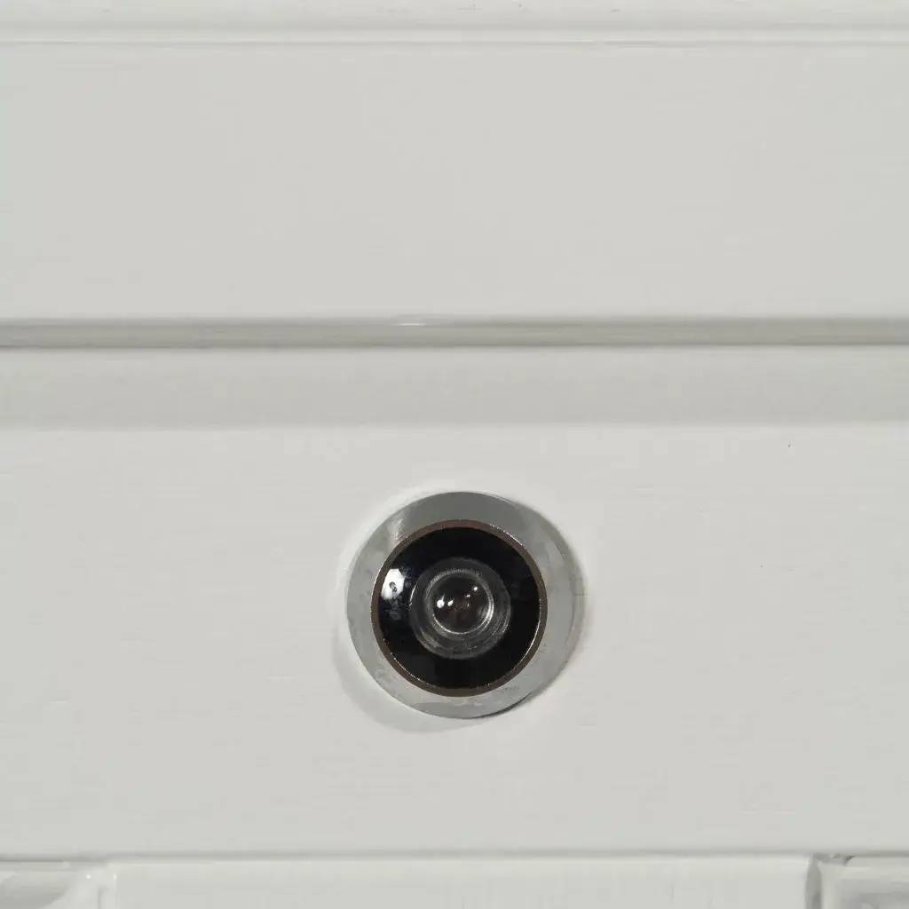 Un judas de porte moderne en métal poli est intégré sur une surface blanche.