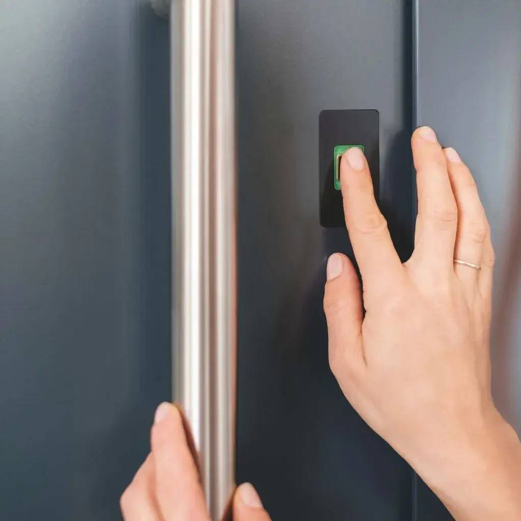 Une main appuie sur un bouton vert sur une porte métallique.