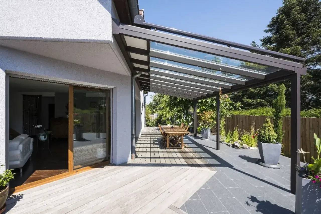 Terrasse moderne et ensoleillée avec une pergola en verre surplombant un espace de détente et de verdure.