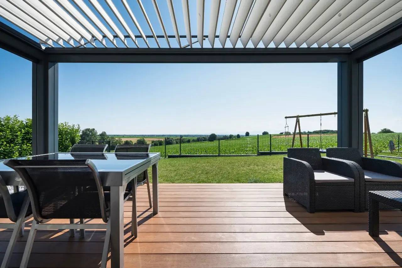 Terrasse moderne avec pergola ouverte sur un jardin verdoyant, offrant une vue imprenable sur la campagne.