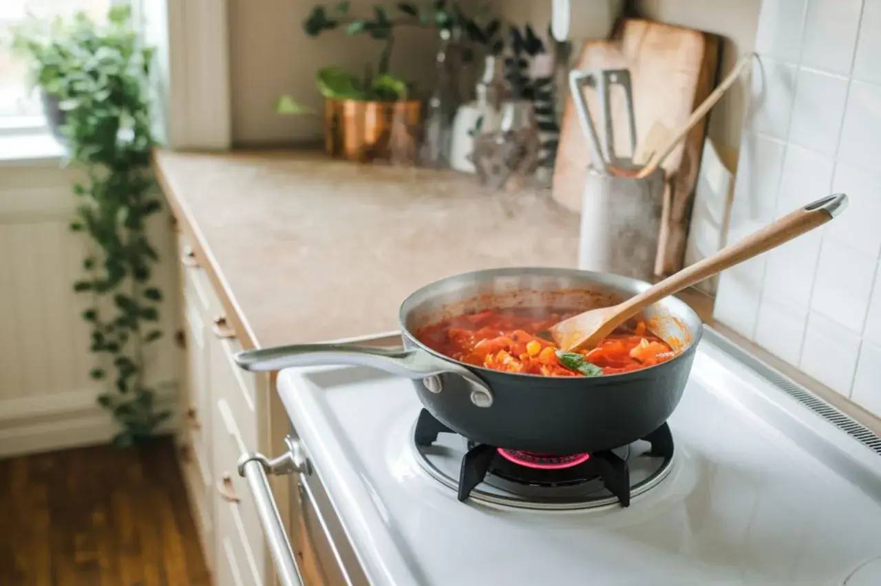 Une casserole de sauce tomate mijote doucement sur une cuisinière dans une cuisine lumineuse et chaleureuse.