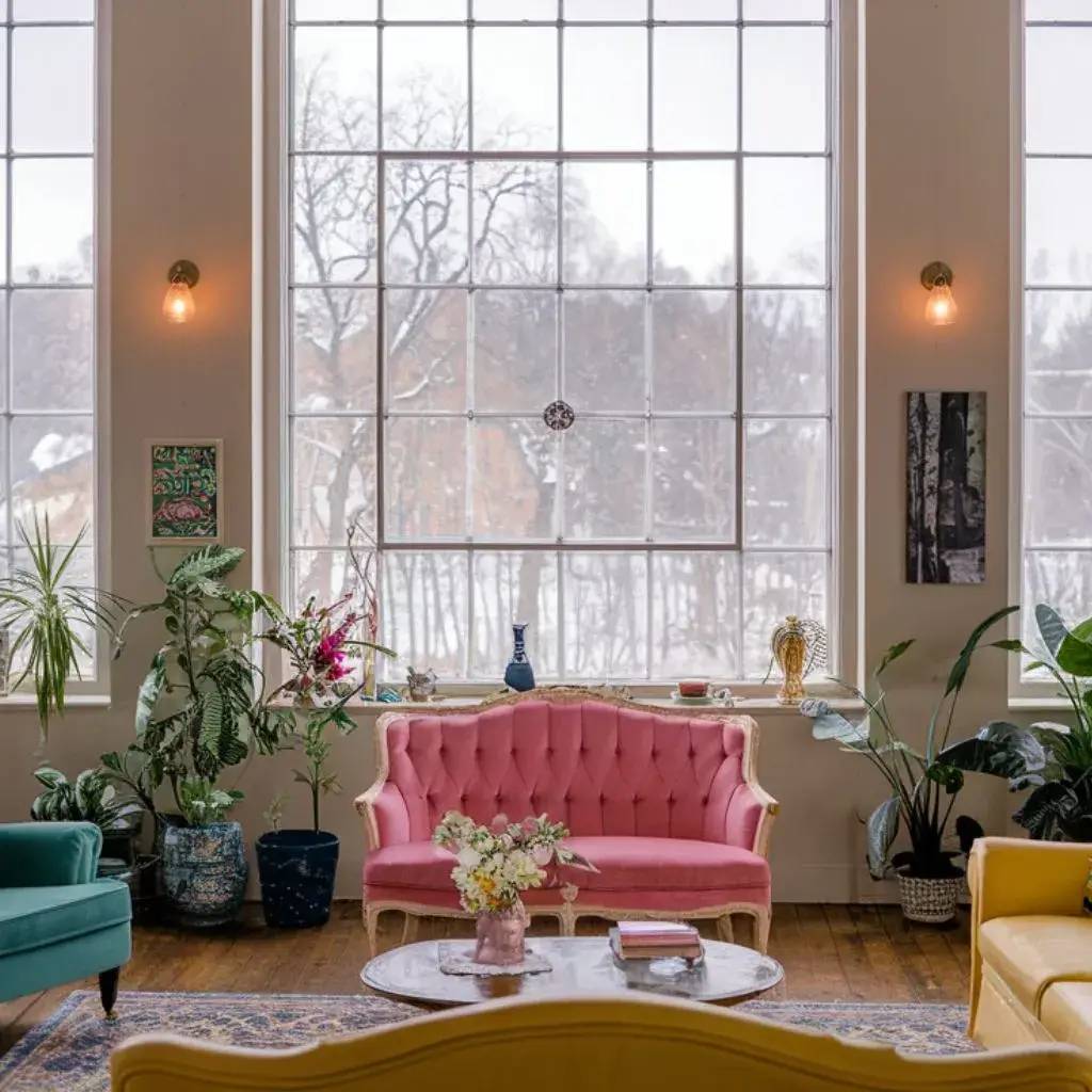 Un salon lumineux avec de grandes fenêtres, décoré de canapés colorés et de plantes d'intérieur.