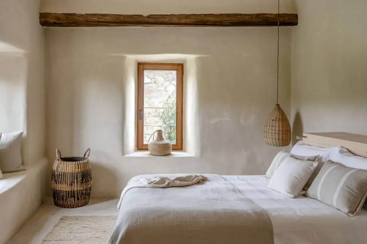 Chambre lumineuse et minimaliste avec des accents naturels, incluant un lit confortable, des murs blancs, et un éclairage suspendu en os