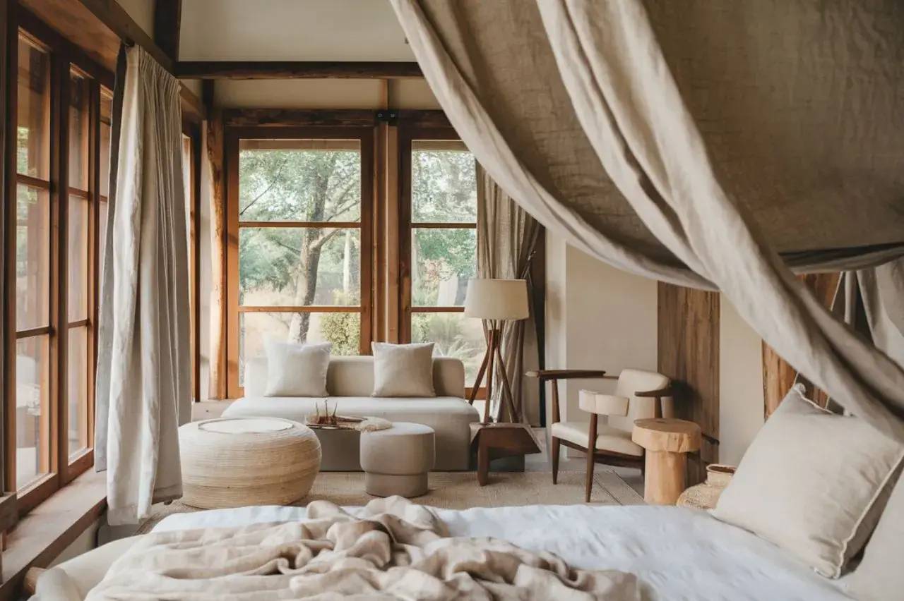 Une chambre lumineuse et élégante avec des fenêtres en bois, des rideaux légers, et un intérieur aux tons naturels.