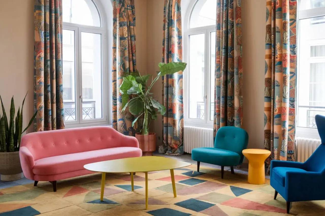 Un salon coloré avec des meubles modernes, comprenant un canapé rose, des fauteuils bleus, et une table basse jaune, entouré de ride