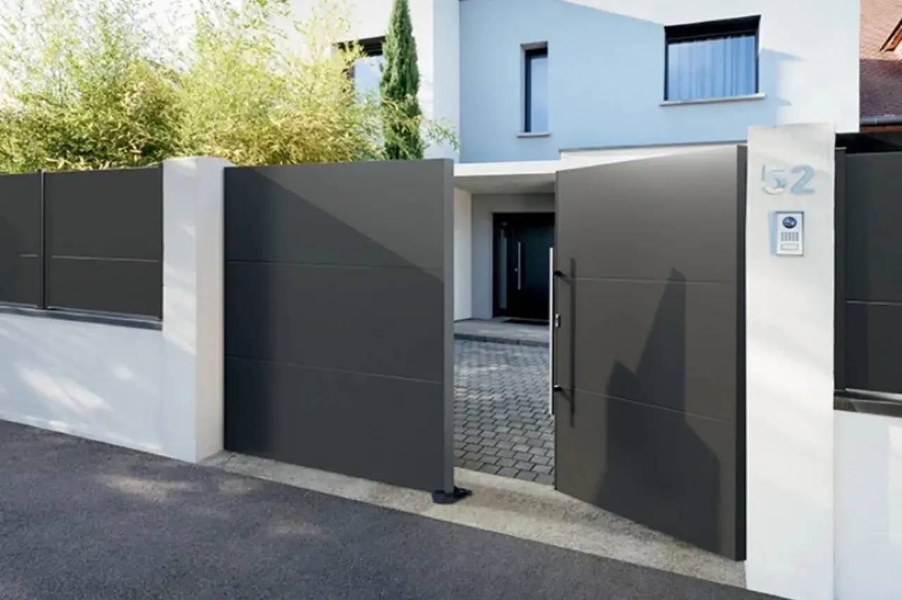 Un portail moderne en métal gris s'ouvre sur une entrée pavée devant une maison contemporaine.