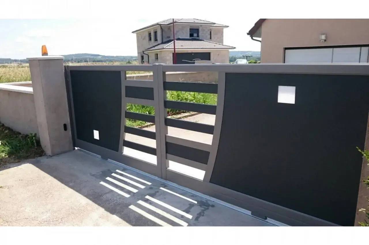 Portail moderne gris en métal, avec design géométrique, devant une maison récente.