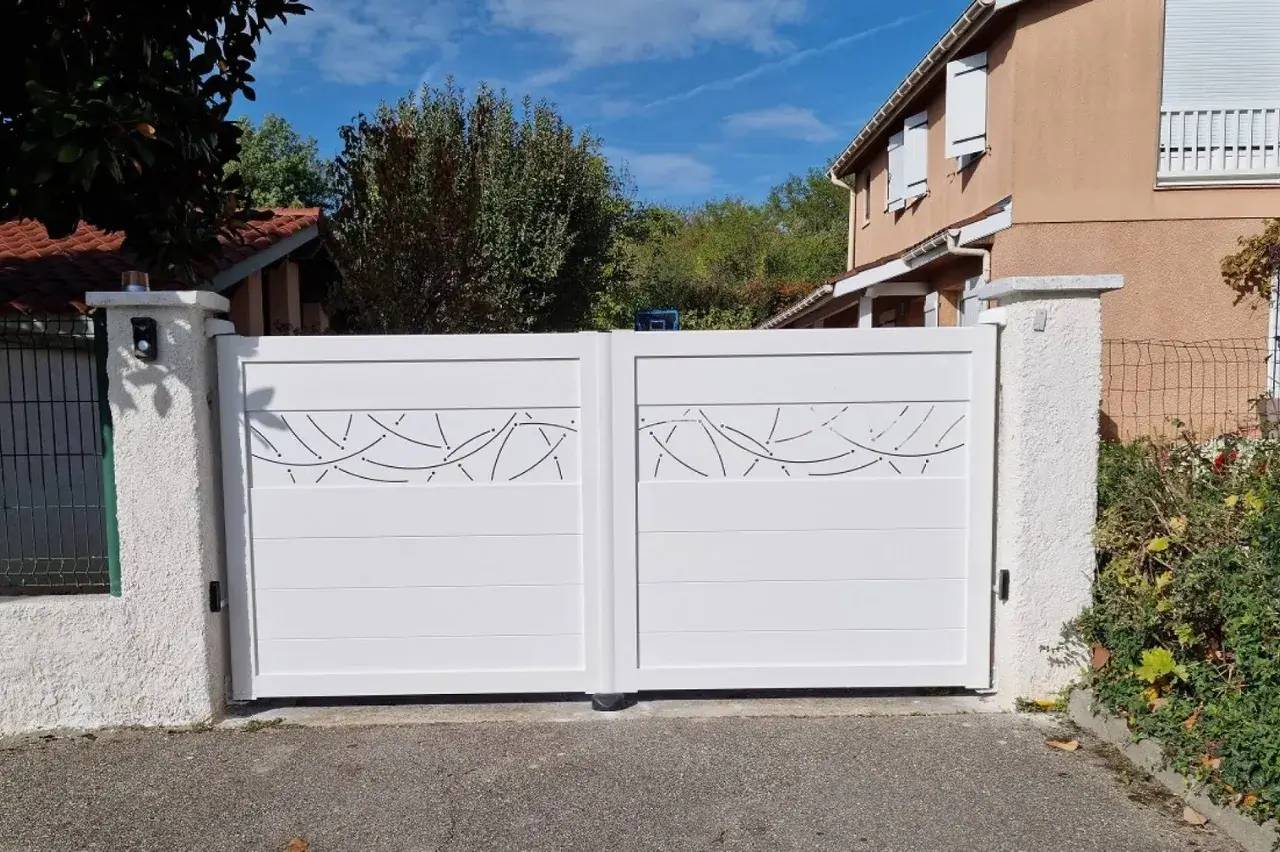 Portail blanc moderne avec motifs ajourés, s'ouvrant sur une maison en arrière-plan.